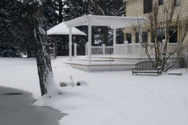 white vinyl pergola over a deck in a snowy backyard with white railings around the deck