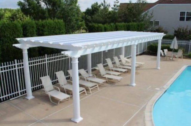 pool chairs under a white tuscany style vinyl pergola beside a pool area