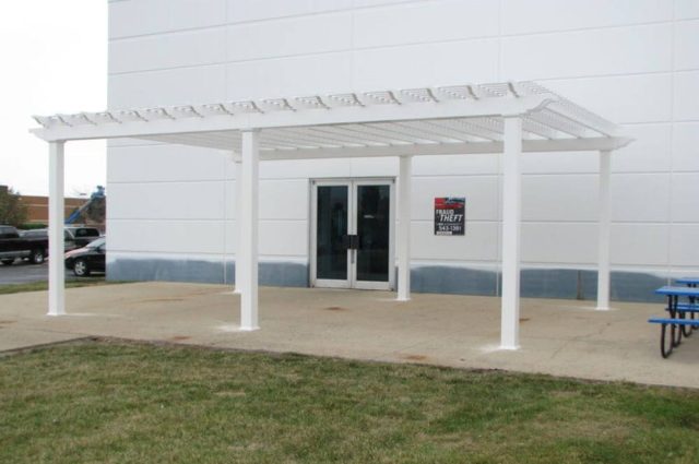 large white pergola with square posts next to a white industrial building