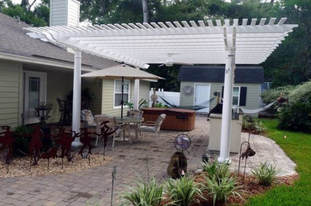 white pergola attached to a house that is also over a backyard patio