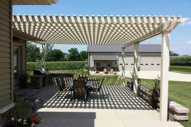 tan pergola attached to home over patio with outdoor furniture on it