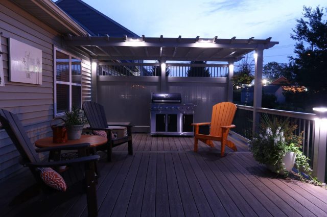 tan vinyl pergola over a wooden deck lit by lights in the dark