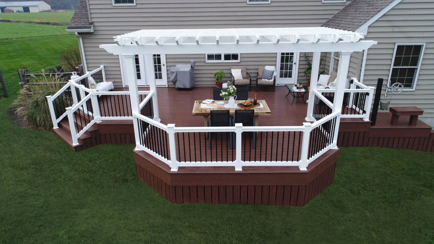 vinyl pergola with attached railings on backyard deck with outdoor furniture and greenery