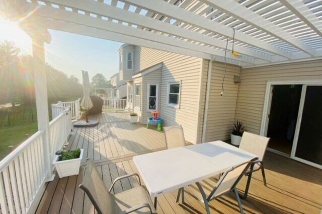 table and chairs on a two story deck with a white pergola over top to keep out the sun